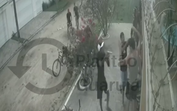 Um dos criminosos aponta uma arma para o casal, que estava em frente à uma residência