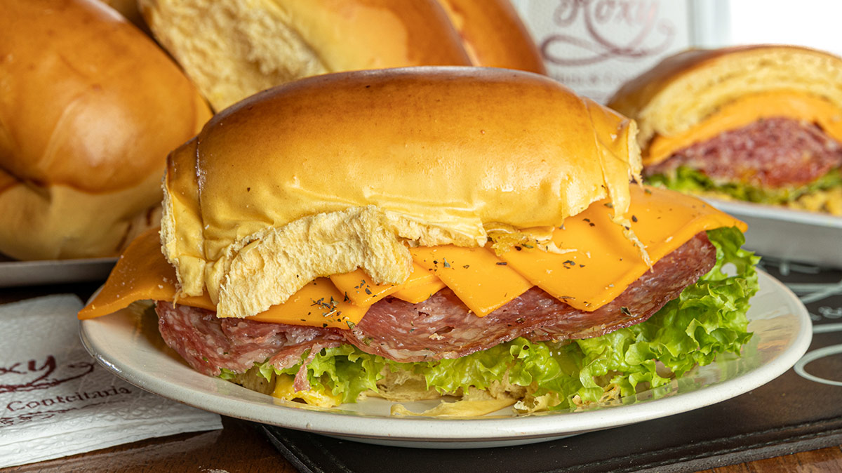Roxy | Cará Melt: Pão de cará tostado no azeite, salame hamburguês, cheddar, alface, tomate temperado com mel, mostarda e orégano