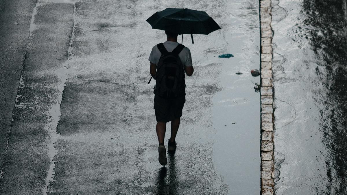 Rapaz caminha segurando um guarda-chuva em dia nublado